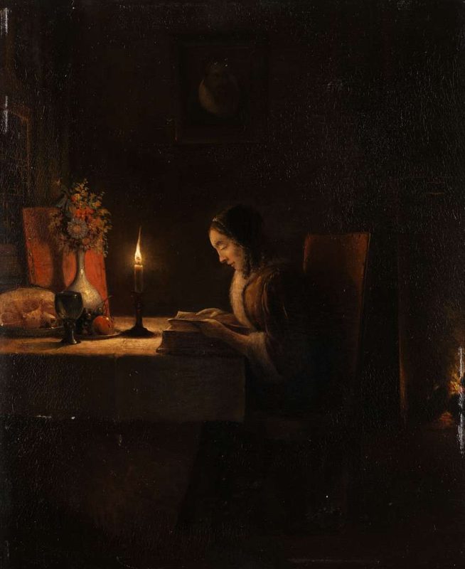 A woman reading at a table by a candle light.
