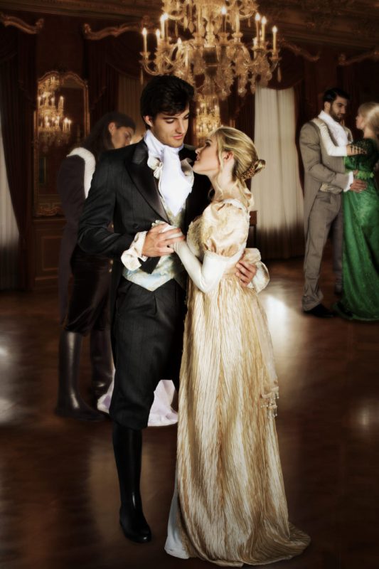 A couple dancing intimately behind a glowing chandelier and other couples.