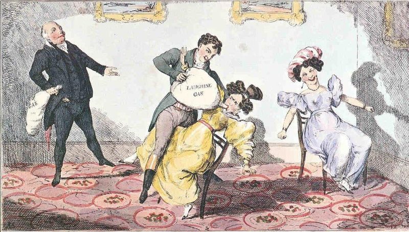 A man holding a laughing gas container that he's trying to get a lady seated on a chair to take in with a couple of individuals around laughing.