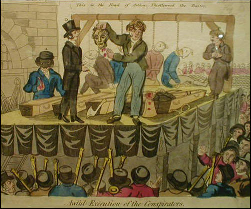 Several men on stage with one holding the head of a man while a few other men can be seen hanged in the background.