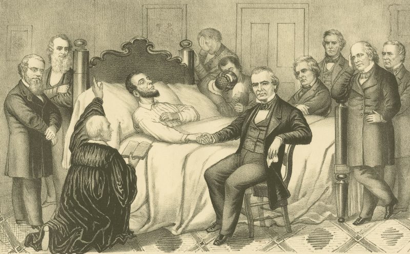 A dying man in bed surrounded by friends and family and a priest raising his arm upon him.