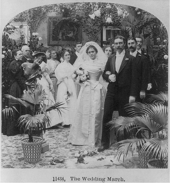 A black and white photo of a bride and groom together with their visitors in a garden.